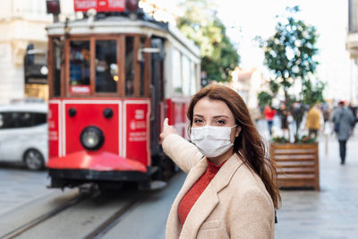 Portrait of woman wearing mask pointing at cable car street in city