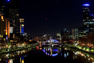 Illuminated buildings by river against sky at night