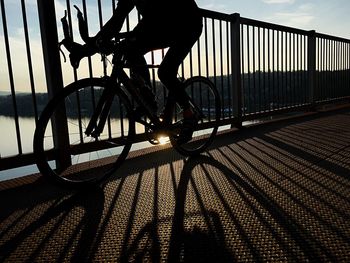 Silhouette person riding bicycle on bridge