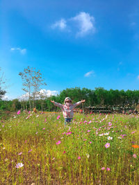 Woman standing on field by flowering plants against sky