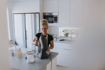 Young woman using stand mixer in kitchen