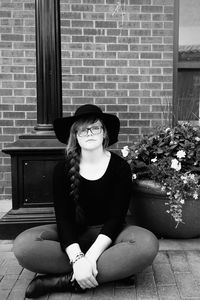 Portrait of smiling woman sitting by plant on footpath