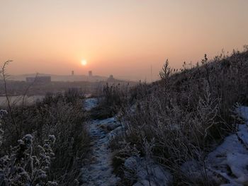 Snow covered land against sky during sunset