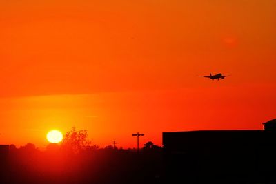 Low angle view of silhouette airplane against orange sky