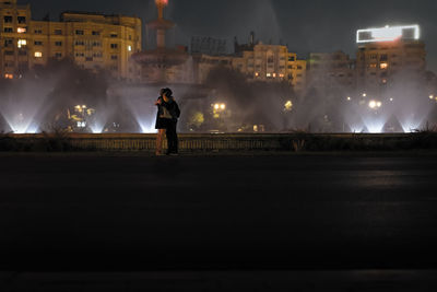 Couple embracing by fountain in city at night