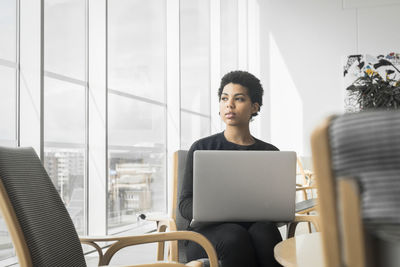 Woman with laptop on lap looking away