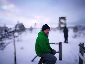 Portrait of man sitting on railing at snow covered field