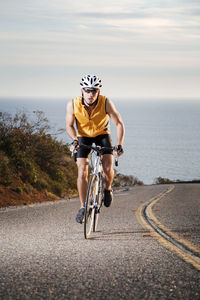 Man cycling on road against sea