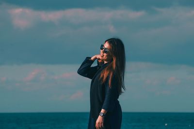 Woman wearing sunglasses standing by sea against sky