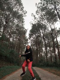 Portrait of young woman standing amidst trees in forest