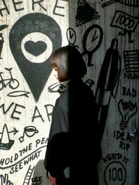 Rear view of woman standing against graffiti wall