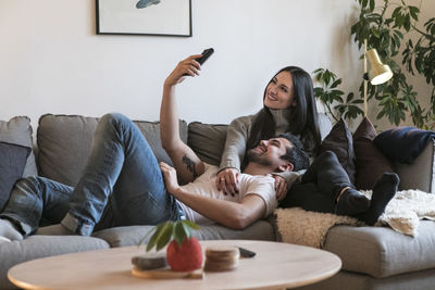 Smiling couple taking selfie on mobile phone while resting on sofa at home