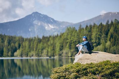 Hiker sitting on rock formation by lake against mountain