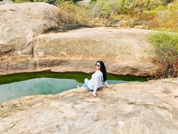 Woman sitting on rock over pond