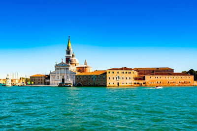 Buildings by sea against clear blue sky