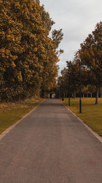 Empty road amidst trees against sky