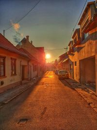 Road amidst buildings against sky during sunset in city