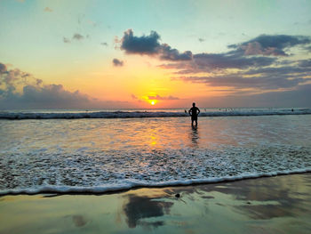 Silhouette people on beach against sky during sunset