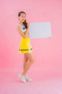 Full length portrait of woman standing against pink background