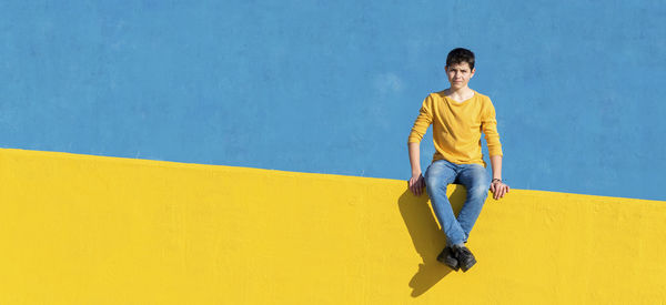 Portrait of boy sitting on yellow railing against blue wall