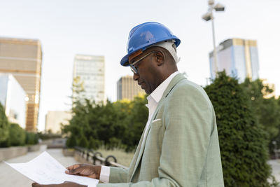 Engineer wearing hardhat examining blueprint at financial district