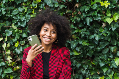 Portrait of a smiling young woman using phone while standing outdoors