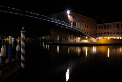 Illuminated buildings by river against sky at night