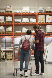 Full length of couple standing with shopping cart in hardware store