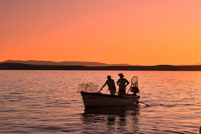 Silhouette men in boat at lake against sky during sunset