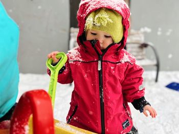 Portrait of a toddler standing on snow while holding a toy spade