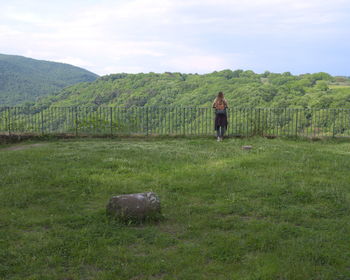 Rear view of woman standing on grassy field by trees against sky