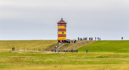 People on field by lighthouse against sky