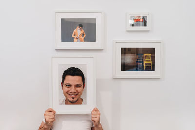 Portrait of man holding frame against wall