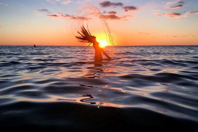 Woman tossing hair in sea during sunset