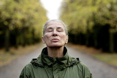 Senior woman with eyes closed wearing raincoat