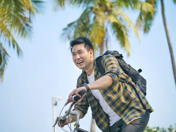 Smiling man sitting on bicycle against palm trees