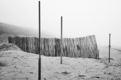 Wooden fence on snow covered field against clear sky