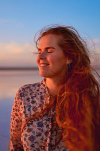 Portrait of young woman looking away against sky during sunset