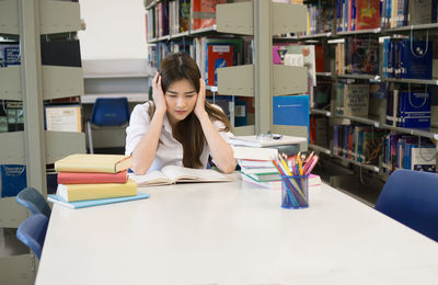 Tensed female student studying at table in library