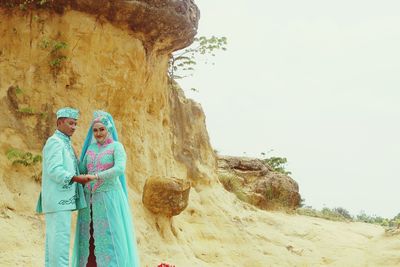 Man and woman wearing traditional clothing while standing by rock formation