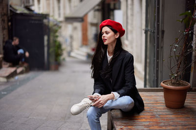 Portrait of young woman sitting on footpath in city
