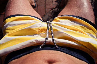 Midsection of shirtless man wearing yellow shorts while resting in yard