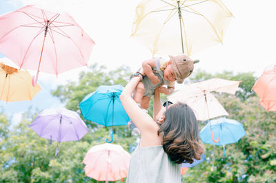 Low angle view of mother picking up son under umbrellas