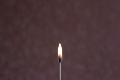 Close-up of burning matchstick against wall