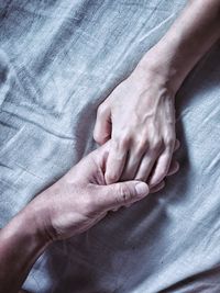 Cropped image of people holding hands on bed