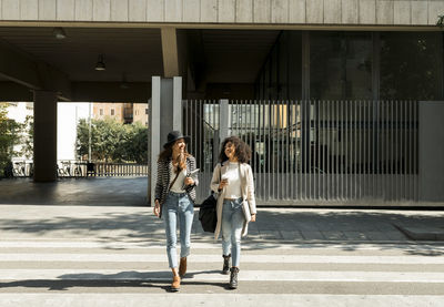 Female colleagues looking away while crossing street in city on sunny day