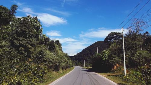 Country road amidst trees against sky