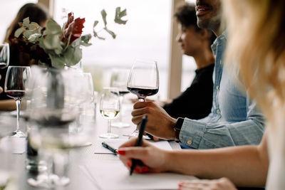 Businessman holding wineglass while sitting with colleagues at table in convention center