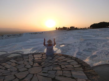 Rear view of man standing on snow covered landscape against sky during sunset