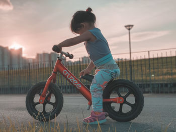 Side view of boy riding bicycle against sky during sunset